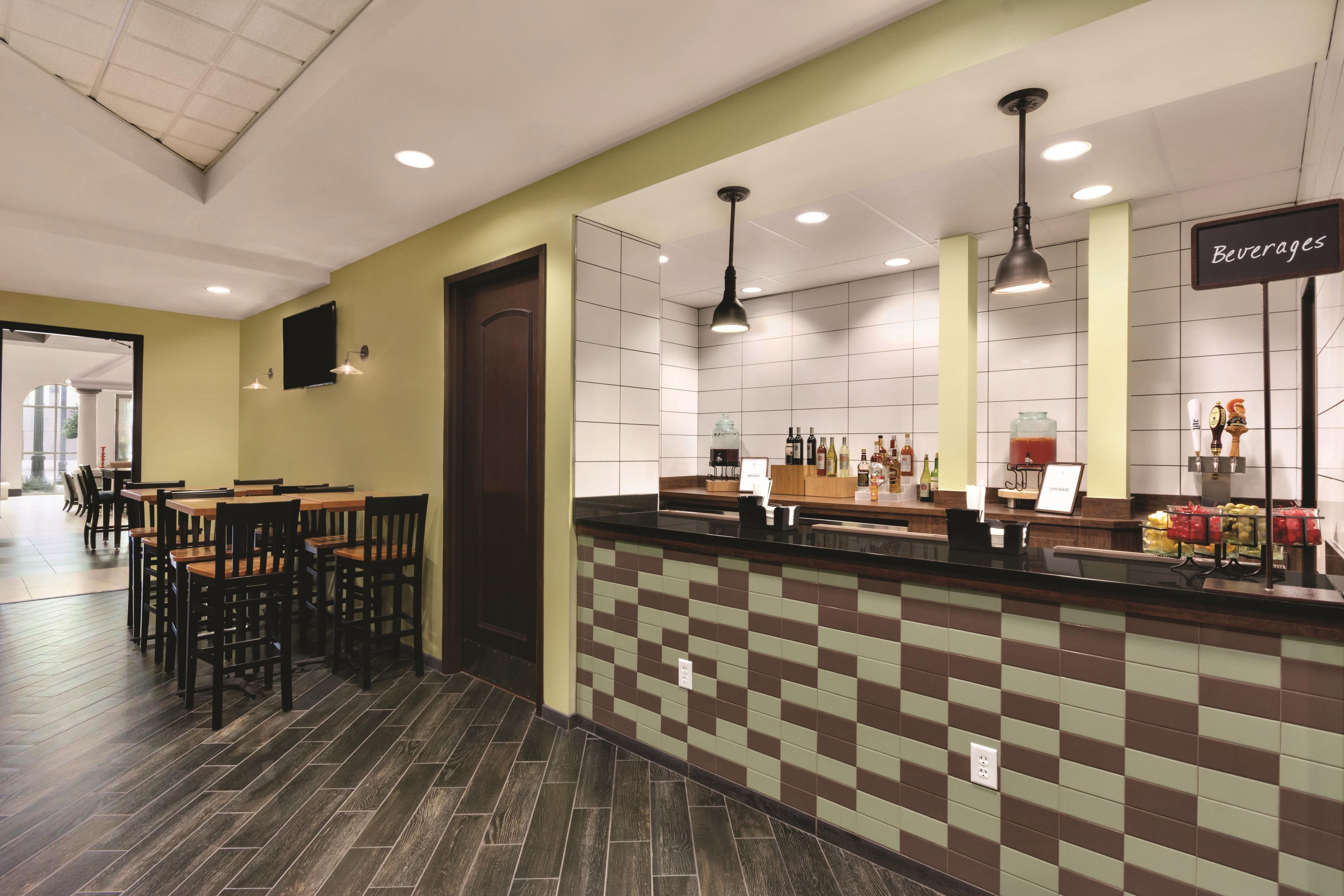A hotel lobby with a reception desk, seating area, and a wall displaying various beverages.