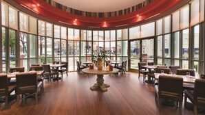 A spacious restaurant with a central round table surrounded by chairs, large windows, and a view of the cityscape. - Embassy Suites by Hilton Tuscaloosa Alabama Downtown (Tuscaloosa)