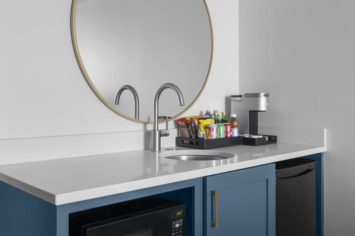 A kitchen with a white countertop, two stainless steel faucets, a coffee maker, and a dish drying rack with various items.