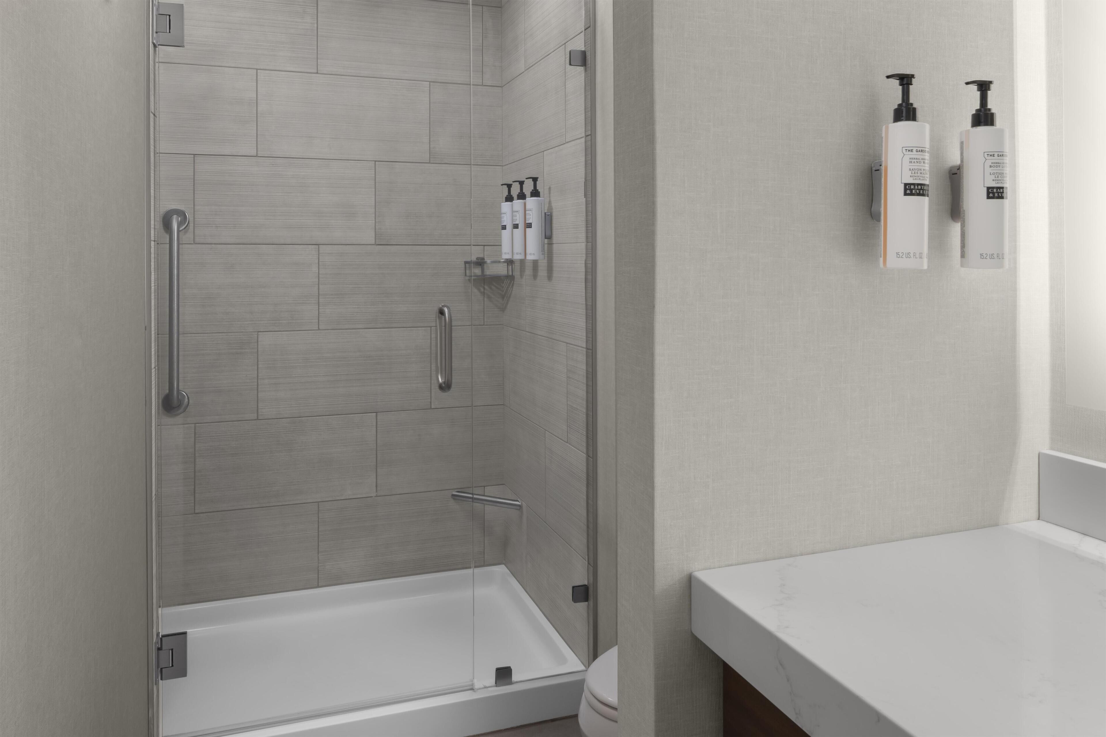 A modern bathroom with a glass-enclosed shower, a white sink, and toiletries on the wall.