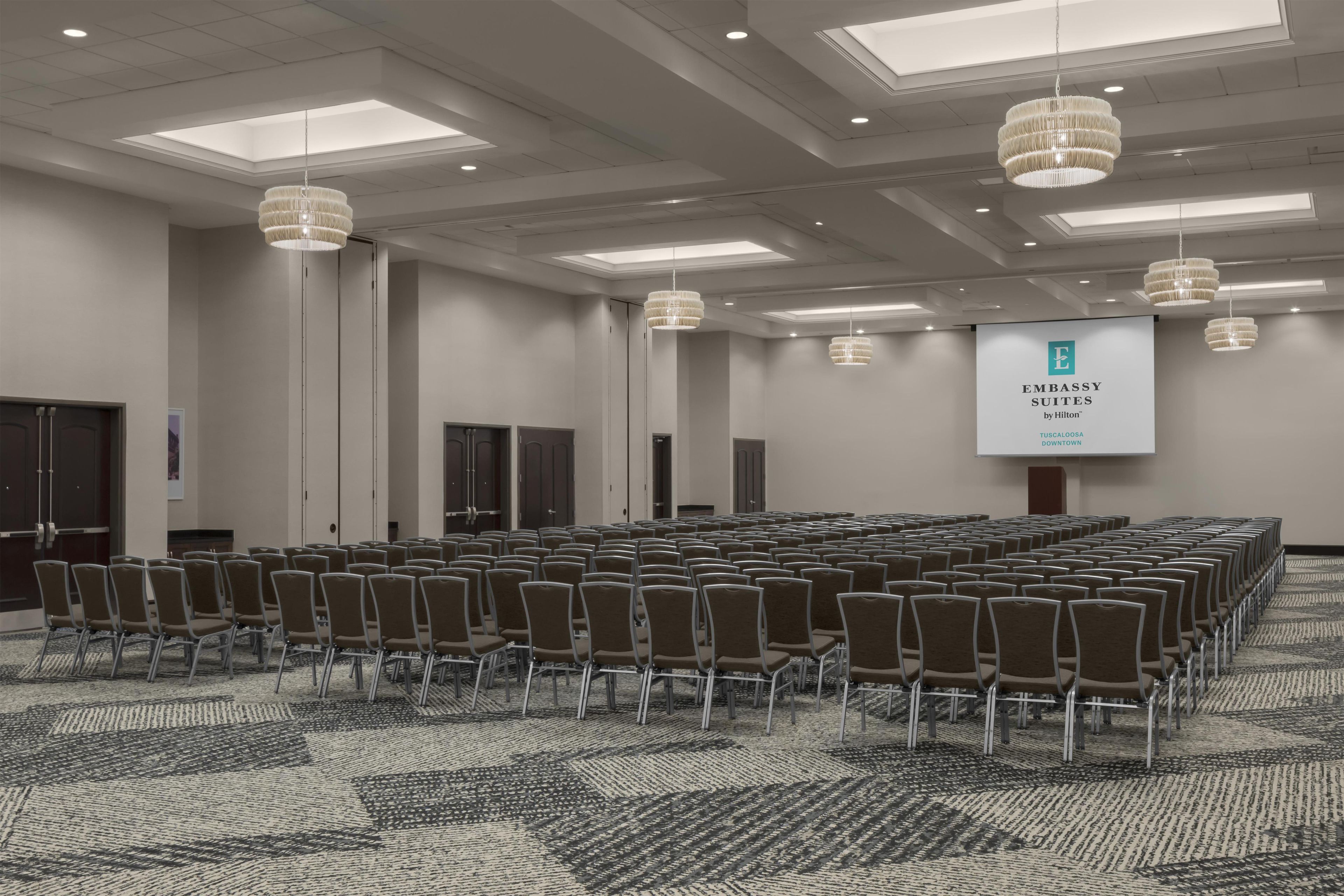 Un salón de conferencias con filas de sillas, una pantalla grande y candelabros.