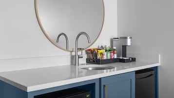 A modern kitchen with a white countertop, two stainless steel faucets, a coffee maker, and a dish drying rack.