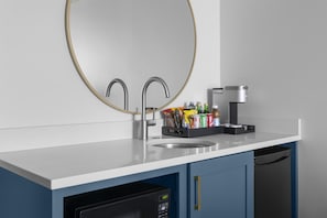 Eine moderne Küche mit weißer Arbeitsplatte, zwei Edelstahlarmaturen, einer Kaffeemaschine und einem Geschirr-Abtropfgestell.