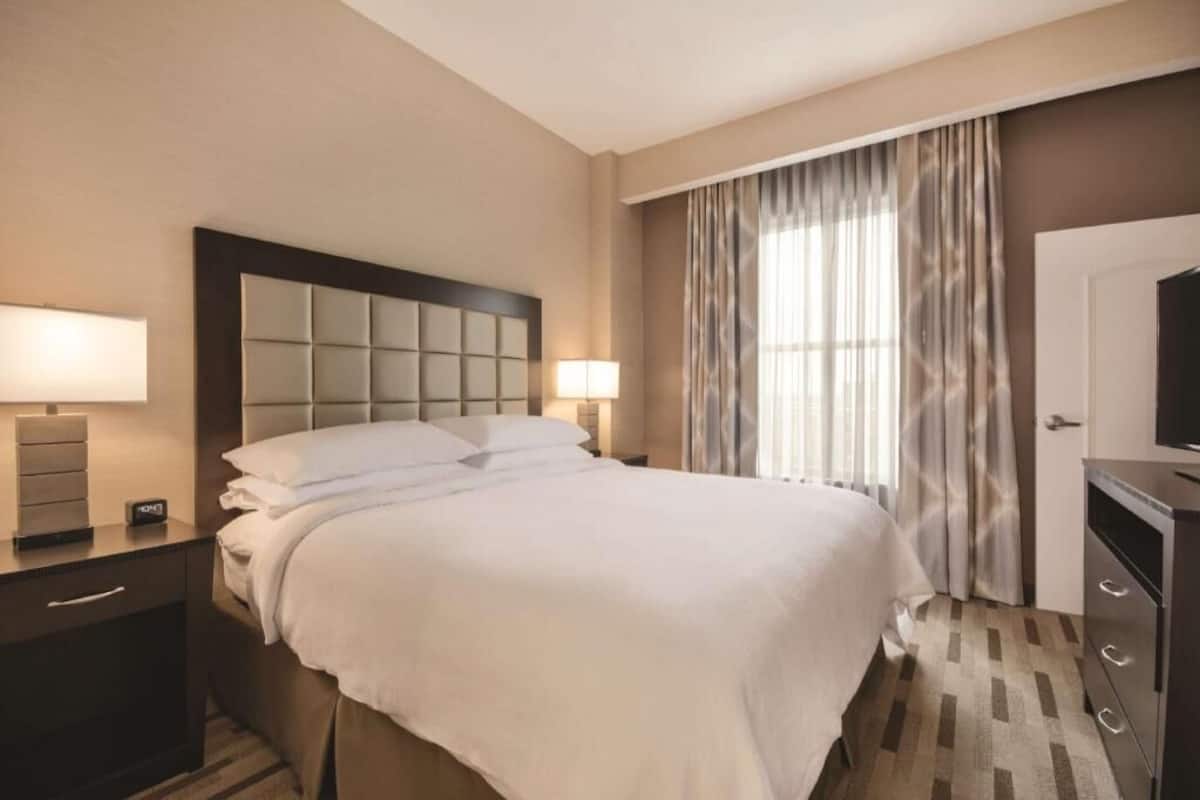 A hotel room with a bed, bedside lamps, a TV, and a door.
