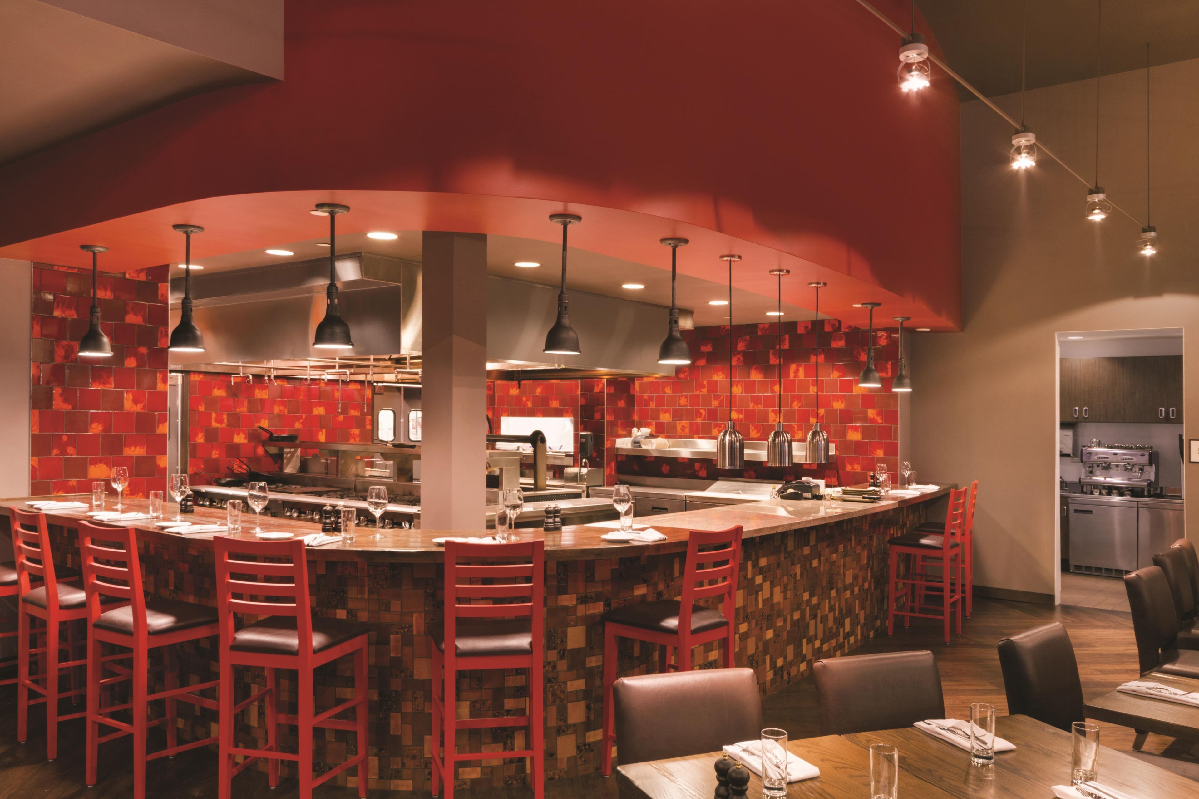 A modern bar area with red chairs, a long counter, and pendant lighting.