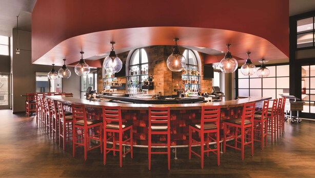 A bar with a curved ceiling, red chairs, and hanging spherical light fixtures. - Embassy Suites by Hilton Tuscaloosa Alabama Downtown (Tuscaloosa)