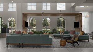 A spacious living area with large windows, a sectional sofa, a coffee table, and a TV mounted on the wall. - Embassy Suites by Hilton Tuscaloosa Alabama Downtown (Tuscaloosa)