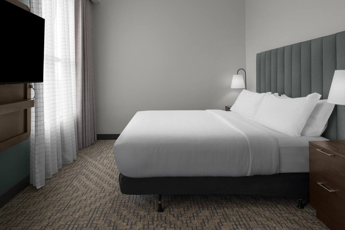 A hotel room with a large bed, a flat-screen TV, a bedside lamp, and a wooden nightstand.