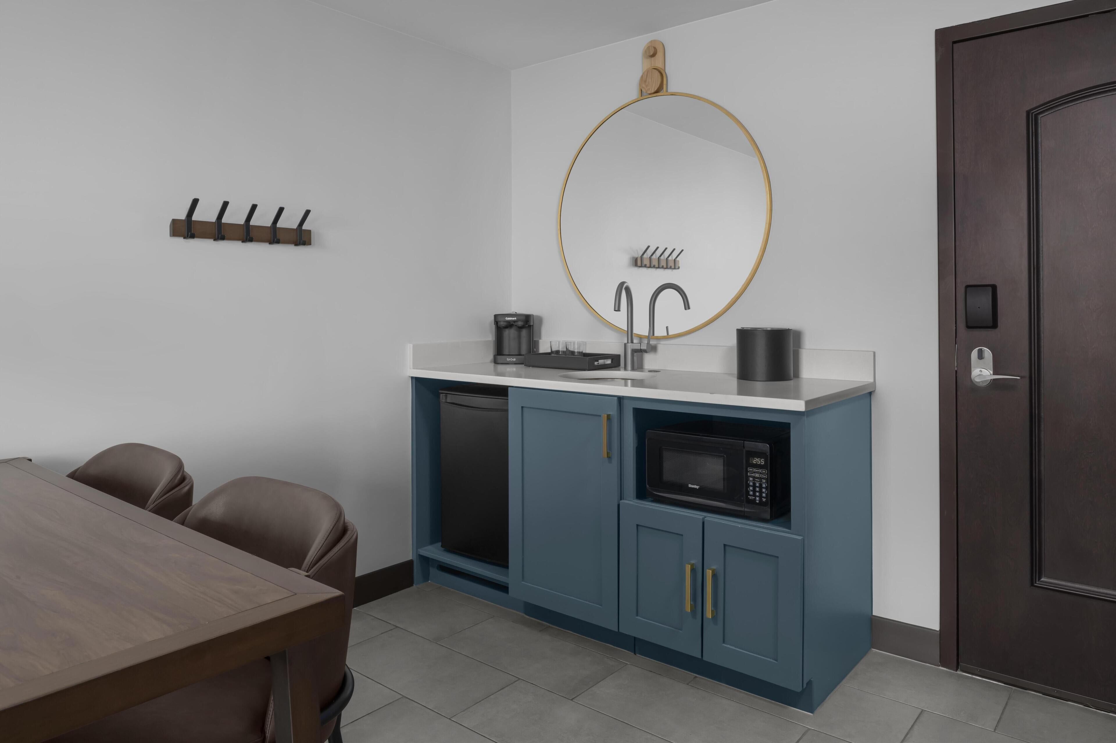 A modern kitchen with a microwave, coffee maker, and a sink. There is a dining table with chairs and a dark door.