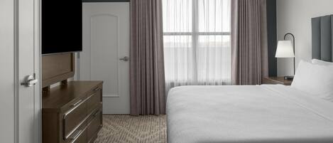 A hotel room with a bed, a TV, a dresser, a lamp, and a window with curtains.