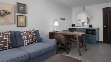 A modern living room with a sofa, a desk, and a kitchen area.