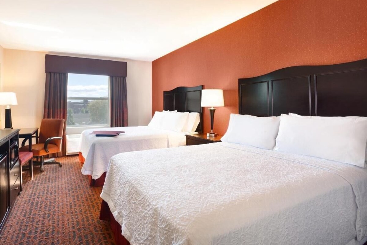 A hotel room with two beds, a desk, a chair, and a window with curtains.