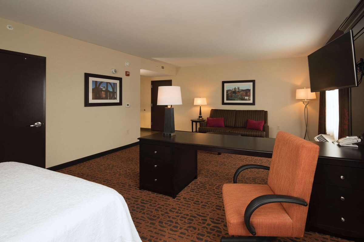 A hotel room with a bed, a desk, a chair, a sofa, a TV, and two lamps.