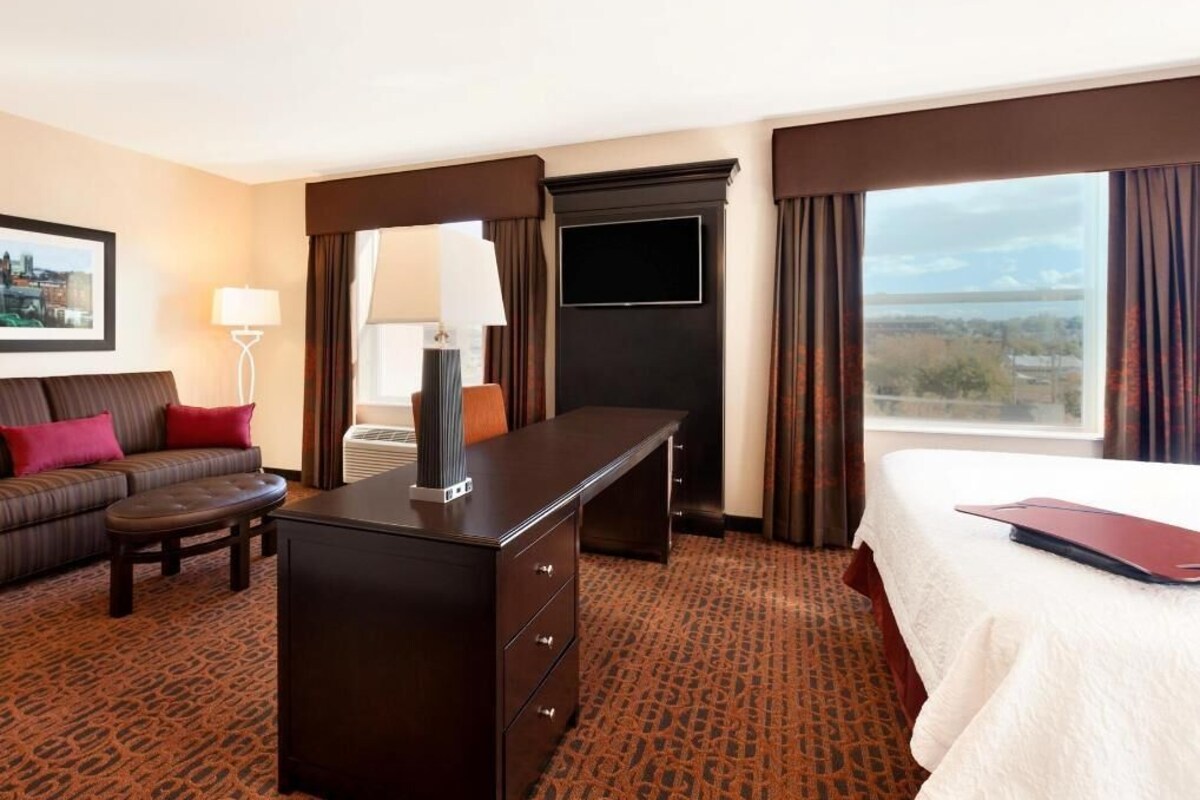 A hotel room with a bed, a desk, a sofa, a TV, and a large window with a view.