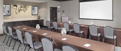A conference room with a long table, chairs, a projector screen, and artwork on the walls.