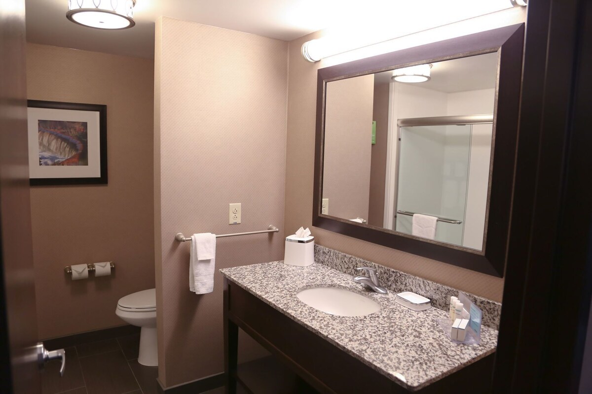 A bathroom with a sink, mirror, towel rack, toilet, and a framed picture on the wall.