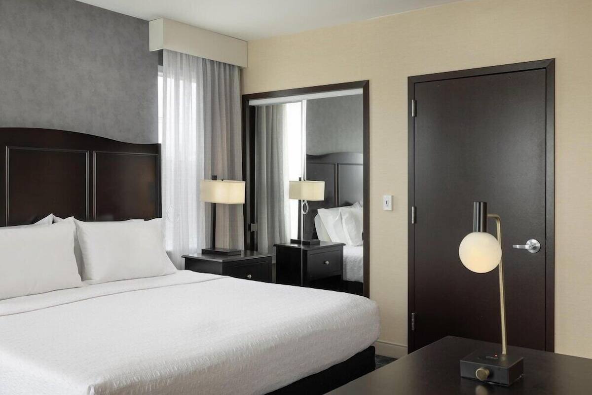 A hotel room with a large bed, a bedside table with a lamp, a wardrobe, and a door.