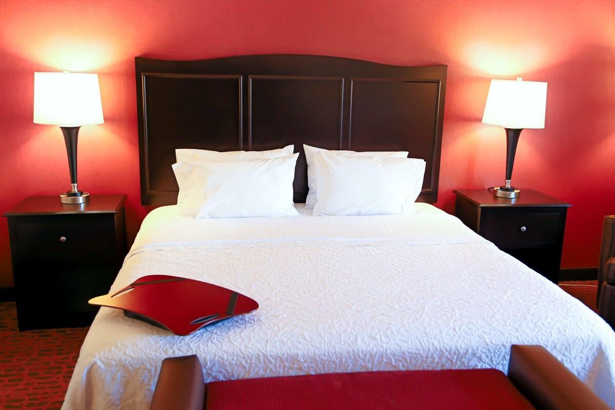 A hotel room with a large bed, two bedside tables with lamps, and a red folder on the bed.