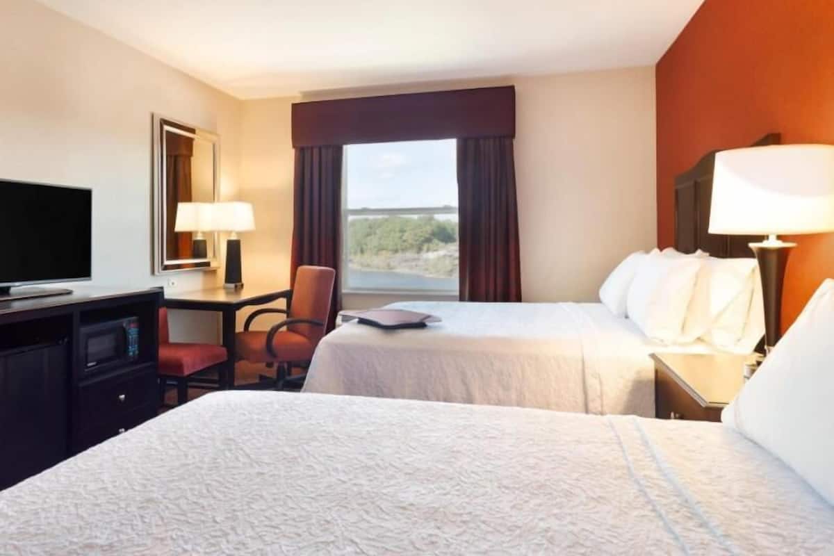 A hotel room with two beds, a TV, a desk, and a window with curtains.