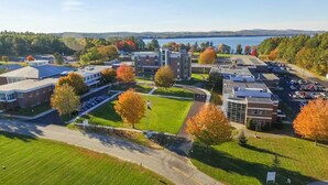 An aerial view of a campus with multiple buildings, parking lots, and a lake in the background. - Hampton Inn Lewiston-Auburn (Lewiston)