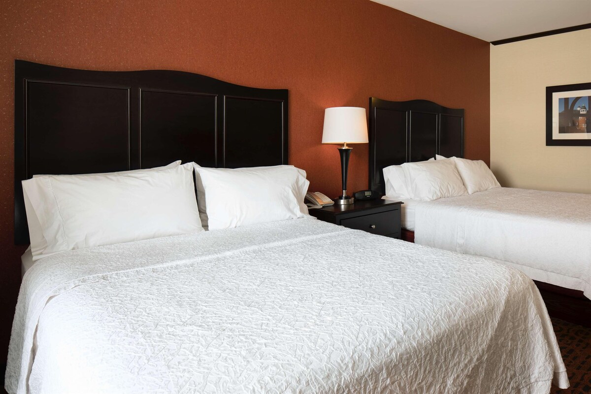 A hotel room with two beds, a nightstand with a lamp, and a framed picture on the wall.