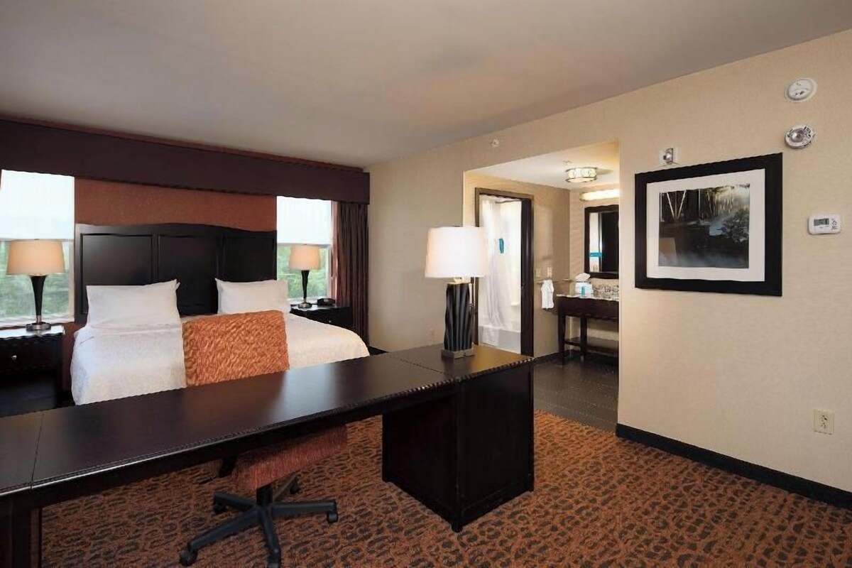 A hotel room with a bed, desk, lamp, and a framed picture on the wall.