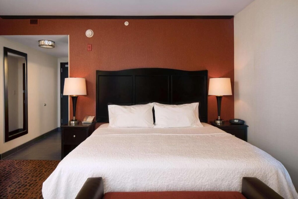 A hotel room with a large bed, two bedside lamps, a headboard, and a carpeted floor.