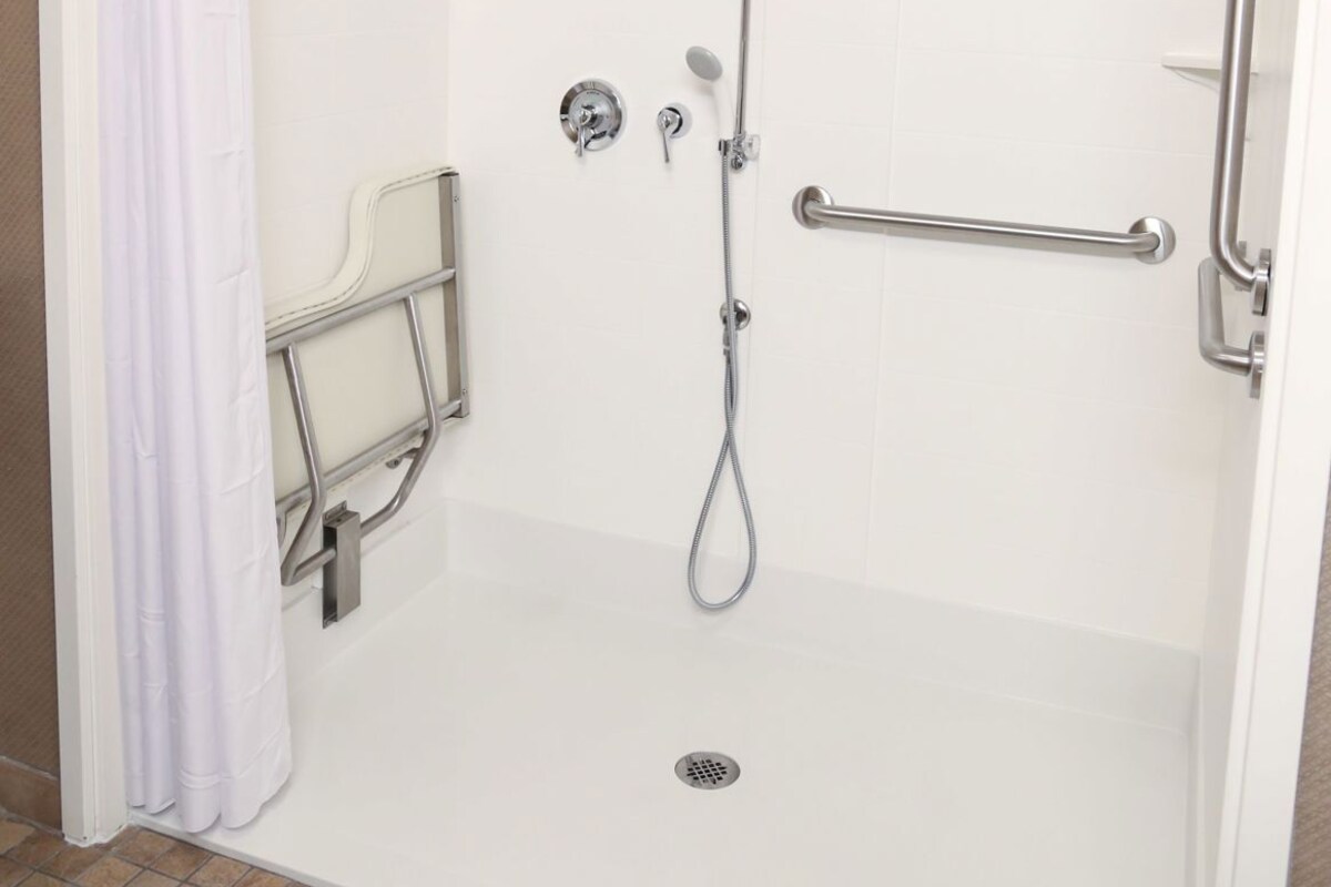 A shower with a grab bar, a showerhead, and a control panel.