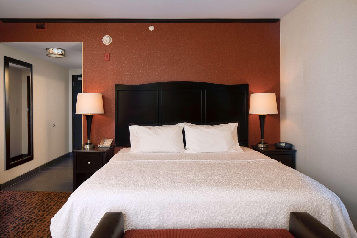 A hotel room with a large bed, two bedside tables with lamps, a headboard, and a carpeted floor.