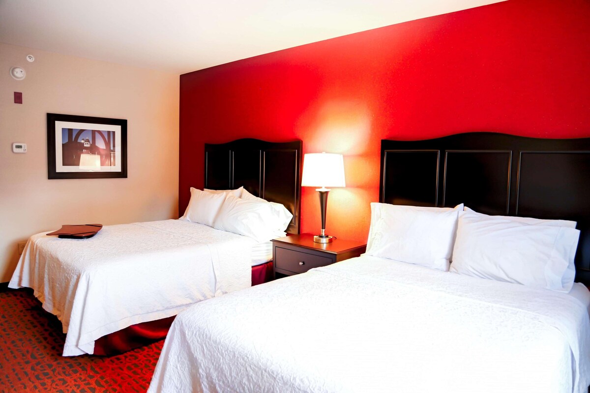 A hotel room with two beds, a nightstand with a lamp, and a framed picture on the wall.