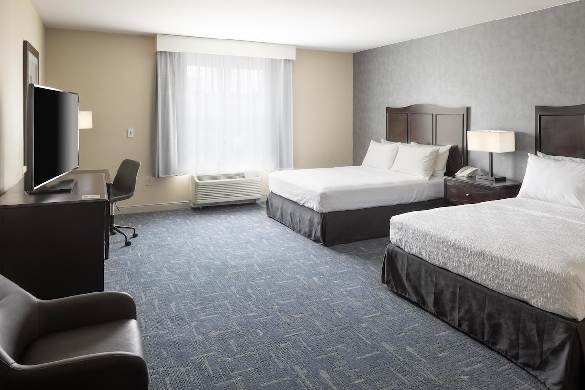 A hotel room with two beds, a desk with a flat-screen TV, a chair, and a window with curtains.