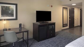 A hotel room with a flat-screen TV, a small refrigerator, a microwave, a desk with a chair, and a bed.