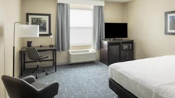A hotel room with a bed, a desk with a chair, a television, and a heater.