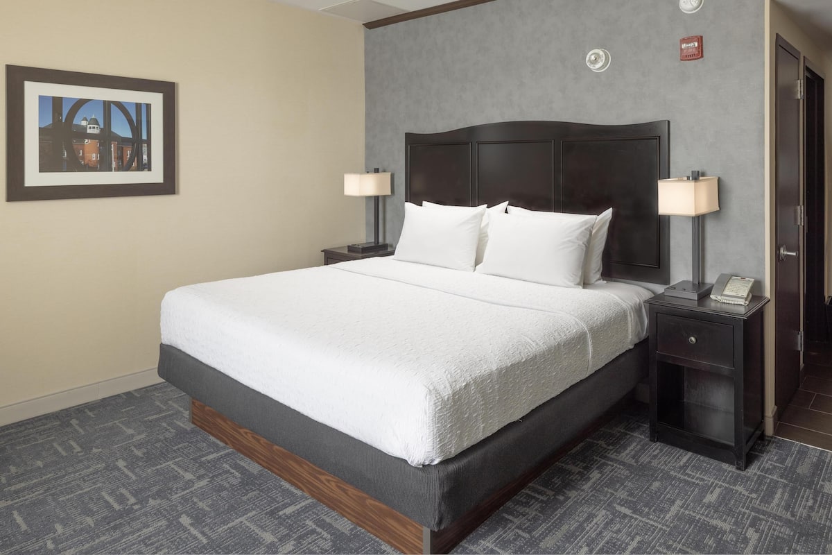 A hotel room with a large bed, two bedside tables with lamps, a framed picture on the wall, and a carpeted floor.