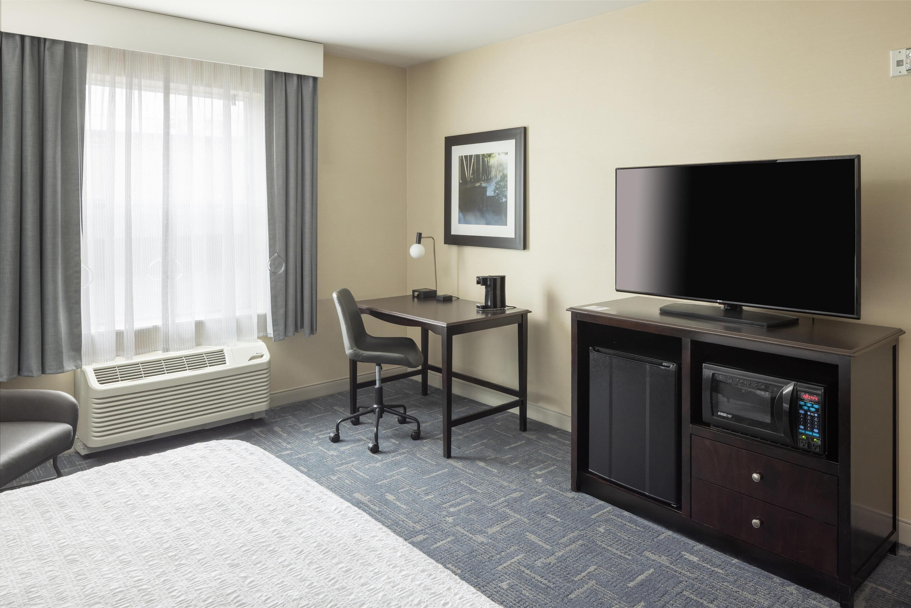 Habitación de hotel con cama, escritorio, silla, televisor, microondas y calefacción.