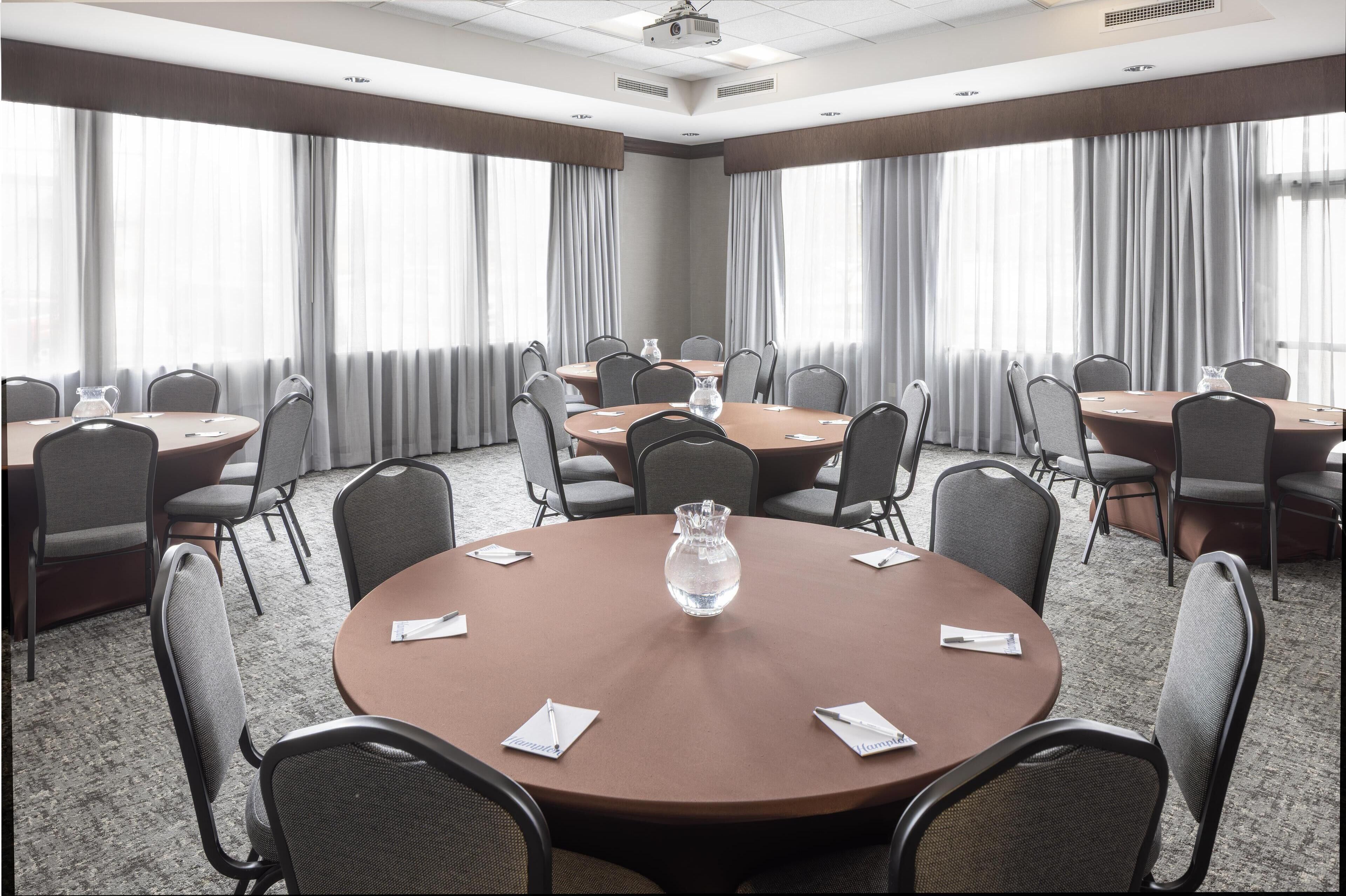 Une salle de conférence équipée de tables rondes, de chaises et d’un projecteur.