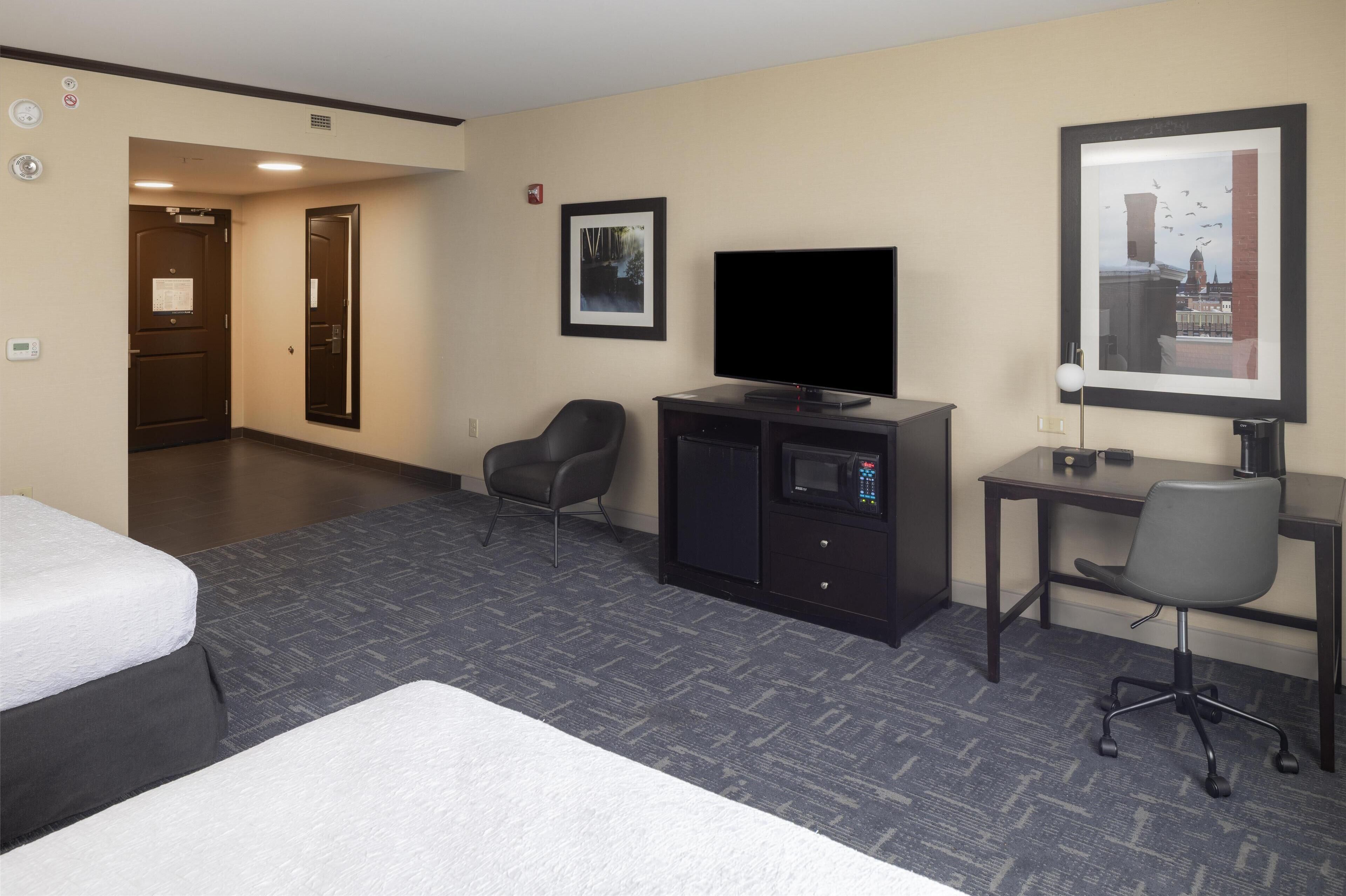 A hotel room with a bed, a desk with a computer, a television, a microwave, and a chair.