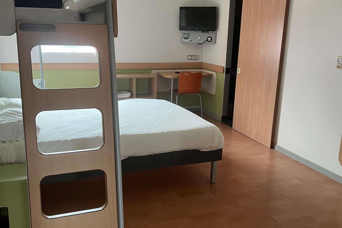 A bunk bed with a desk and chair, a television, and a small table with a chair.