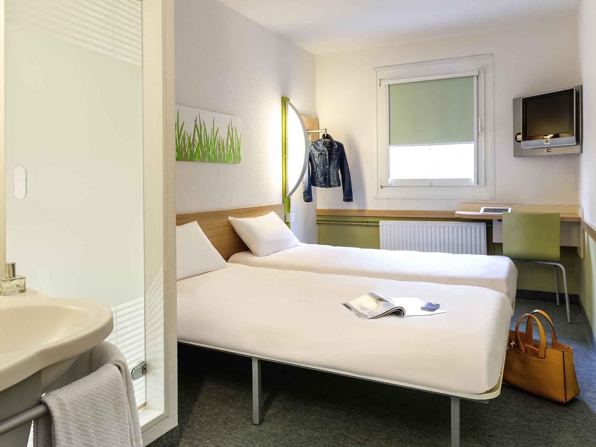 Una camera d'albergo con due letti, una scrivania, uno specchio, una televisione e un bagno.