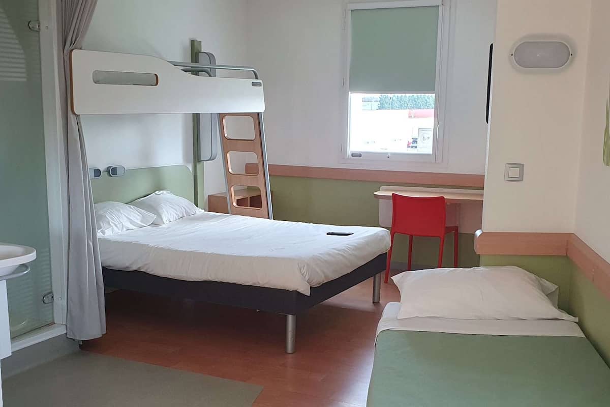 A room with a bunk bed, a desk, a chair, and a window.