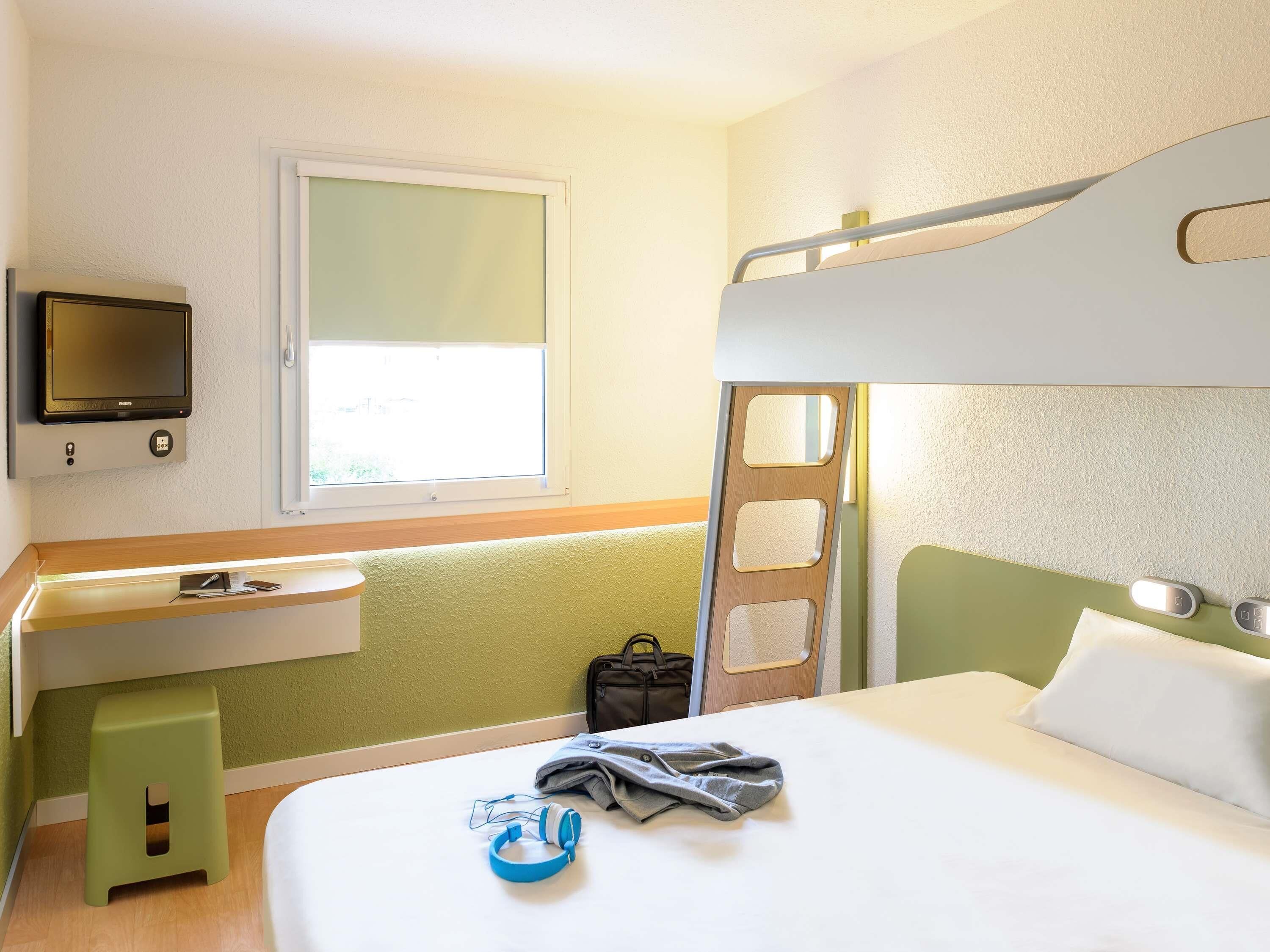 A bunk bed room with a television, a desk, and a window.