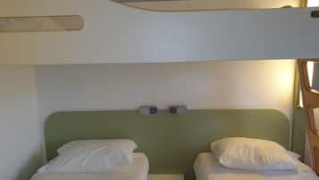 Ein kleines Zimmer mit zwei Einzelbetten, einem grünen Kopfteil und einem kleinen Nachttisch.