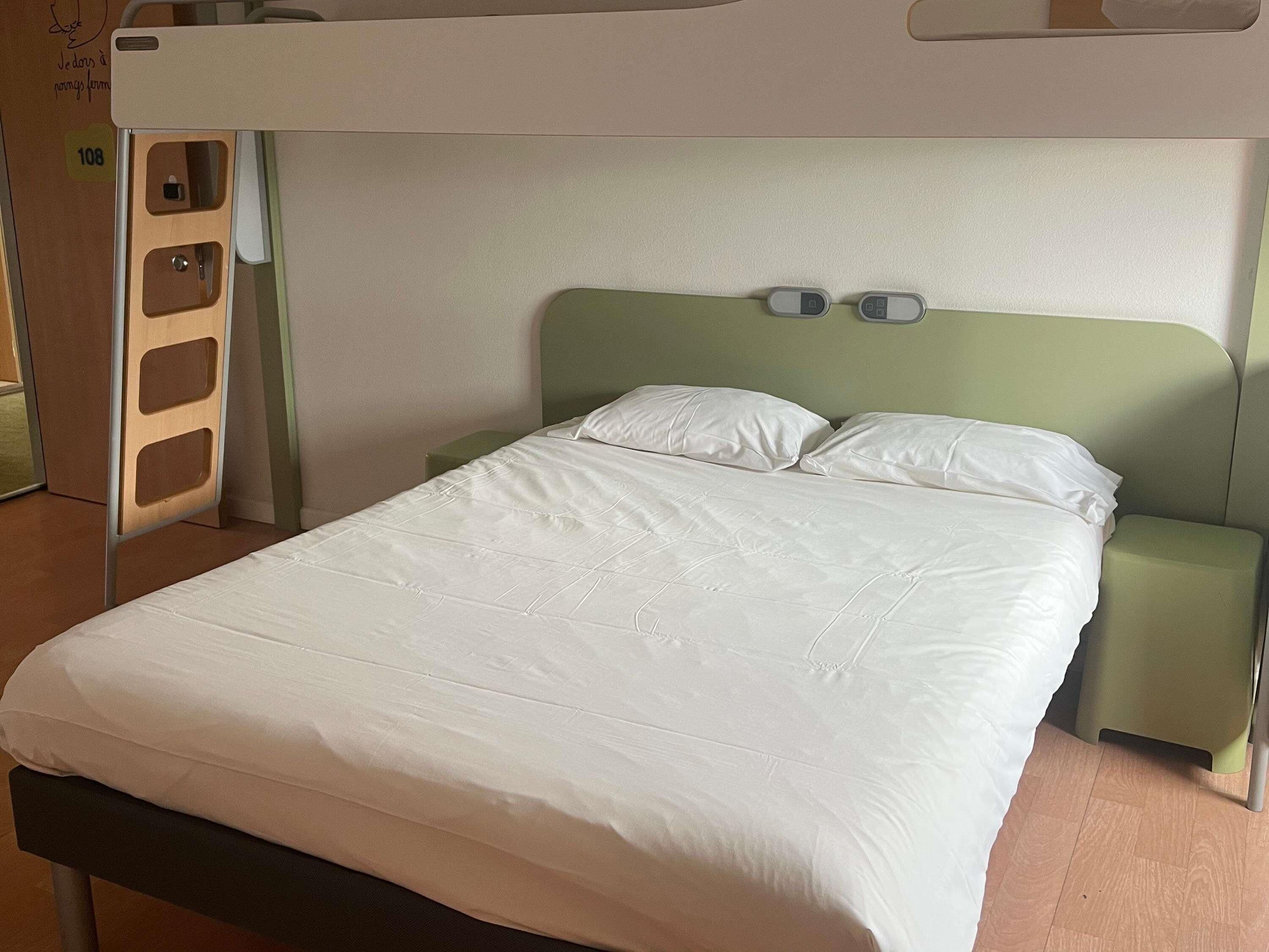 A single bed with a green headboard, white bedding, and a small bedside table with a lamp.
