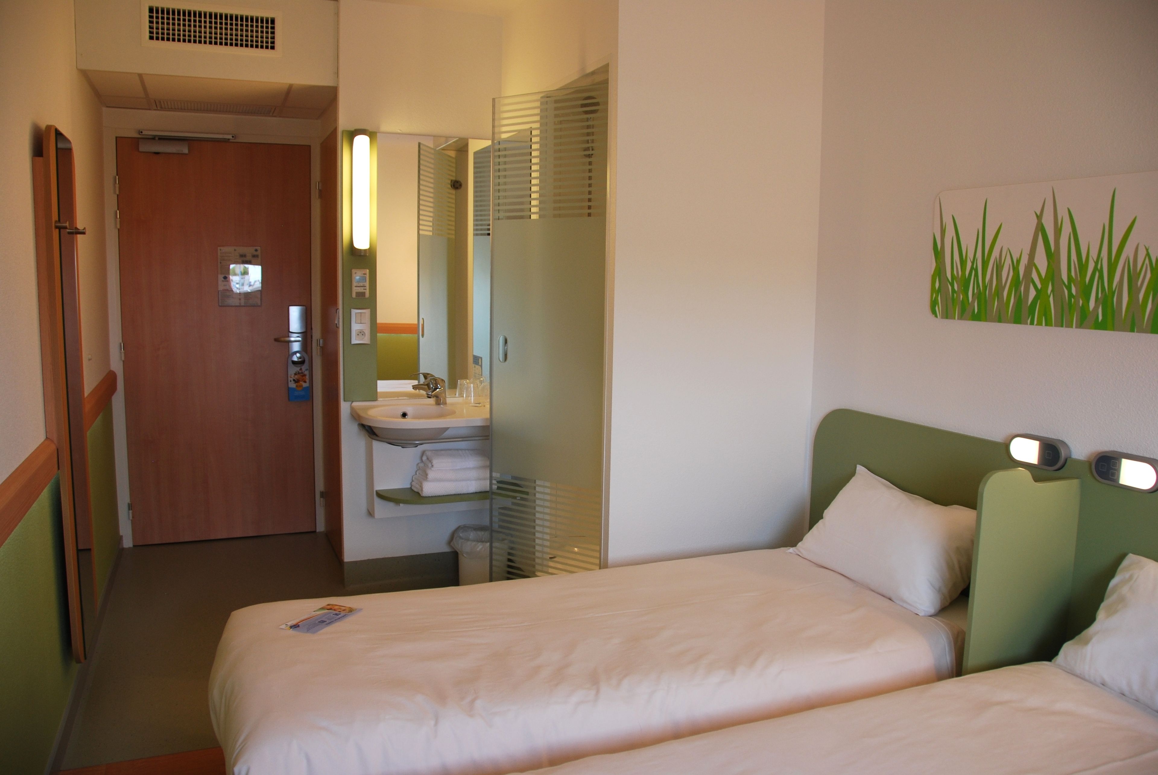 Een hotelkamer met twee bedden, een badkamer met een wastafel en een spiegel.
