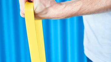 A person holding a yellow resistance band against a blue background.