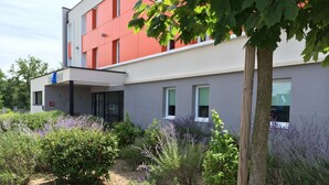 Un edificio moderno con fachada roja, un acceso cubierto y un jardín con diversas plantas.