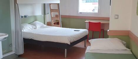 A room with a bunk bed, a desk, a chair, a window, and a bathroom.