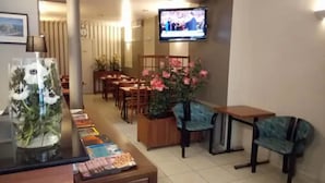 A hotel lobby with a TV mounted on the wall, a reception desk, several tables and chairs, and a large floral arrangement. - Liberty (Paris)