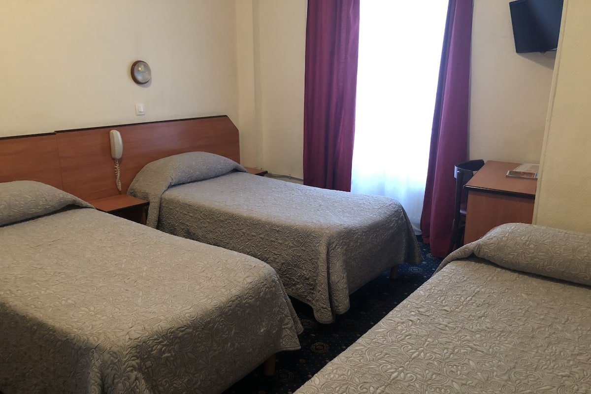 Une chambre d’hôtel avec deux lits simples, une tête de lit en bois, une table de chevet avec un téléphone et un petit bureau avec une chaise.