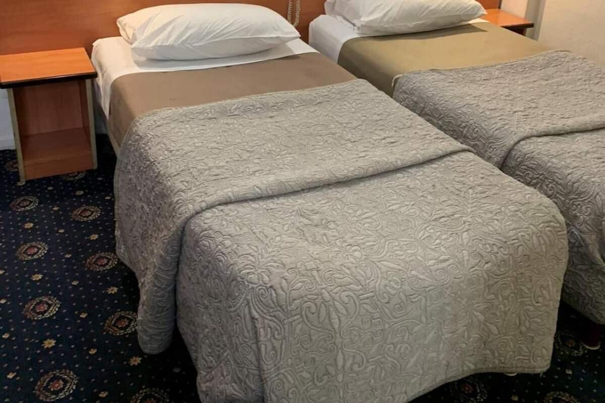 Une chambre d’hôtel avec deux lits simples, chacun doté d’une tête de lit en bois et d’une table de chevet. Un téléphone est fixé au mur, entre les deux lits.